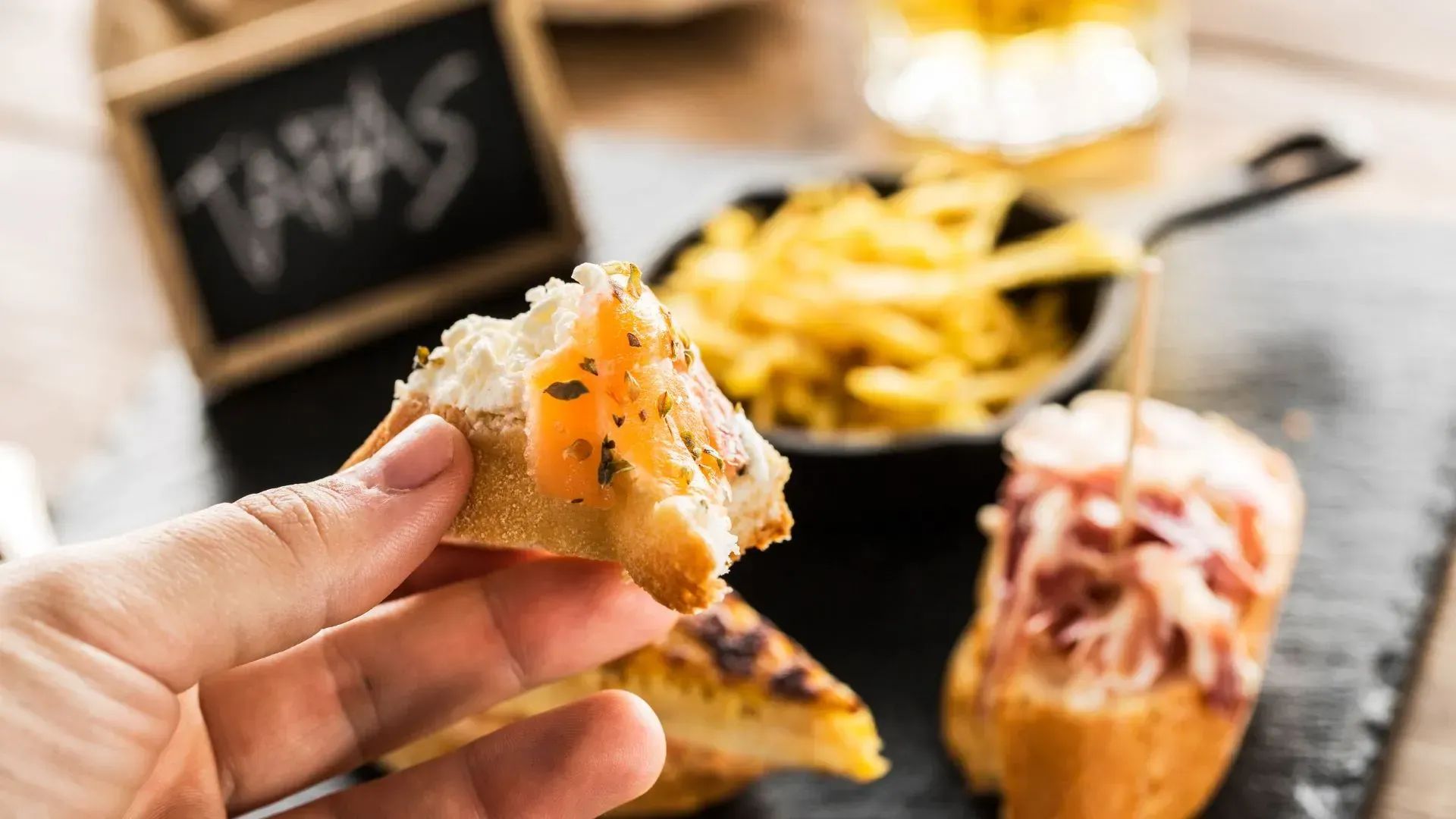 Interior de restaurante con mesas y sillas de madera, paredes de piedra y suelo de baldosas.