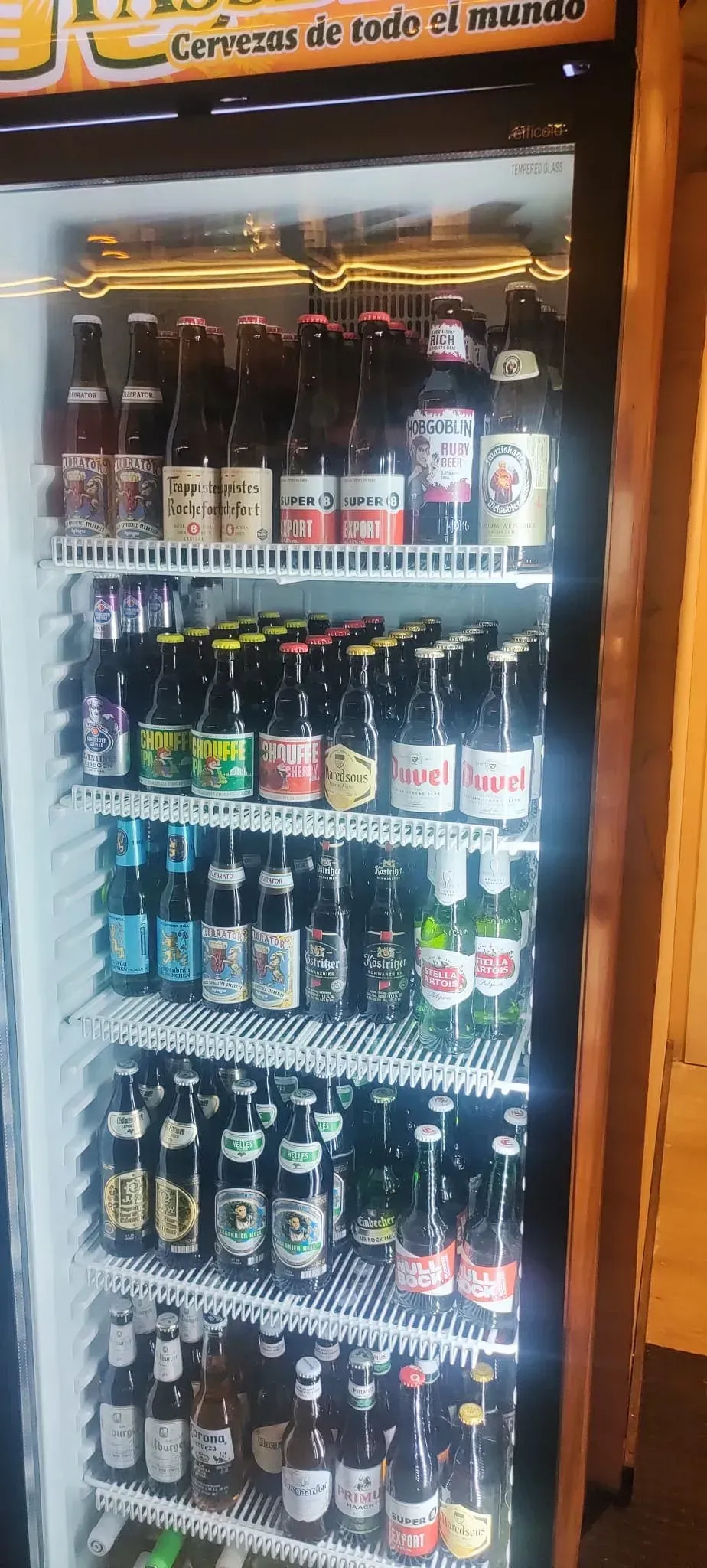 Una vitrina refrigerada repleta de filas de botellas de cerveza de vidrio de diferentes variedades.