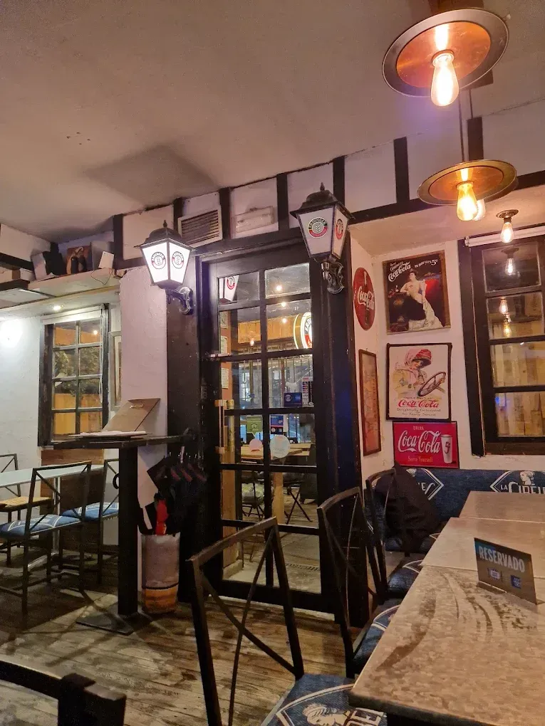 Vista interior de un restaurante con iluminación tenue, con una puerta de cristal, faroles colgantes y carteles antiguos de Coca-Cola.