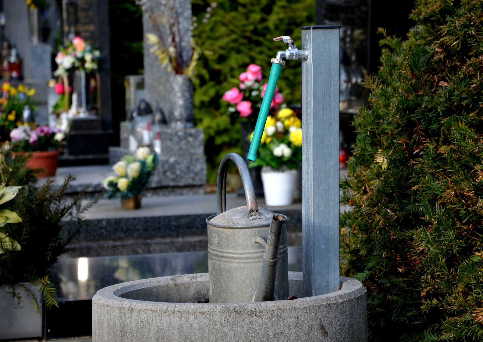 Un arrosoire devant un robinet dans un cimetière