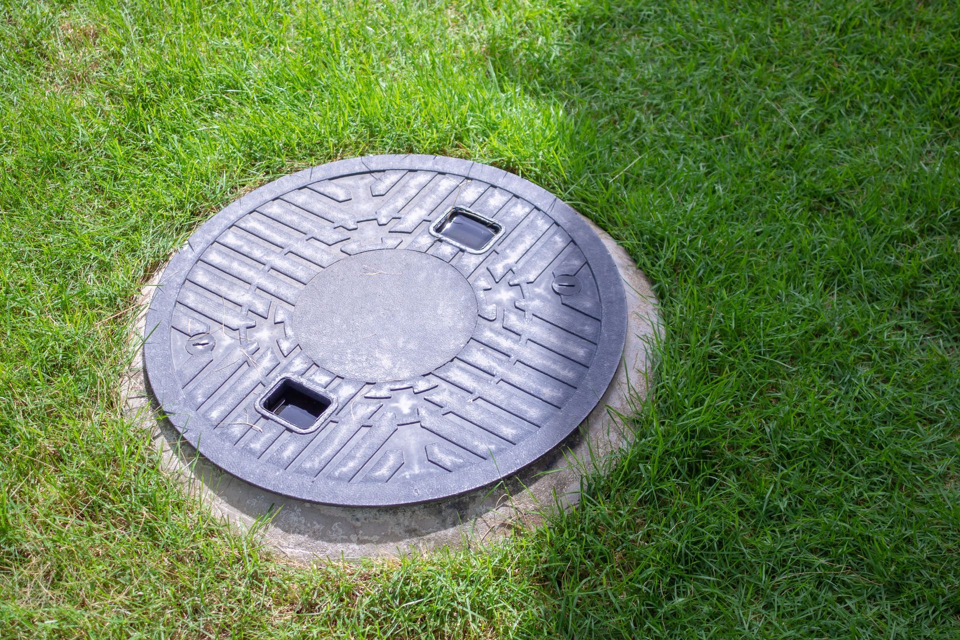 Un couvercle de fosse septique entouré d'herbe.