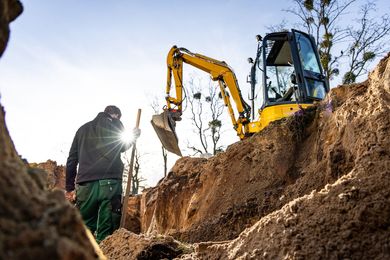 Ouvrier du bâtiment à côté d'une pelleteuse jaune creusant une tranchée.