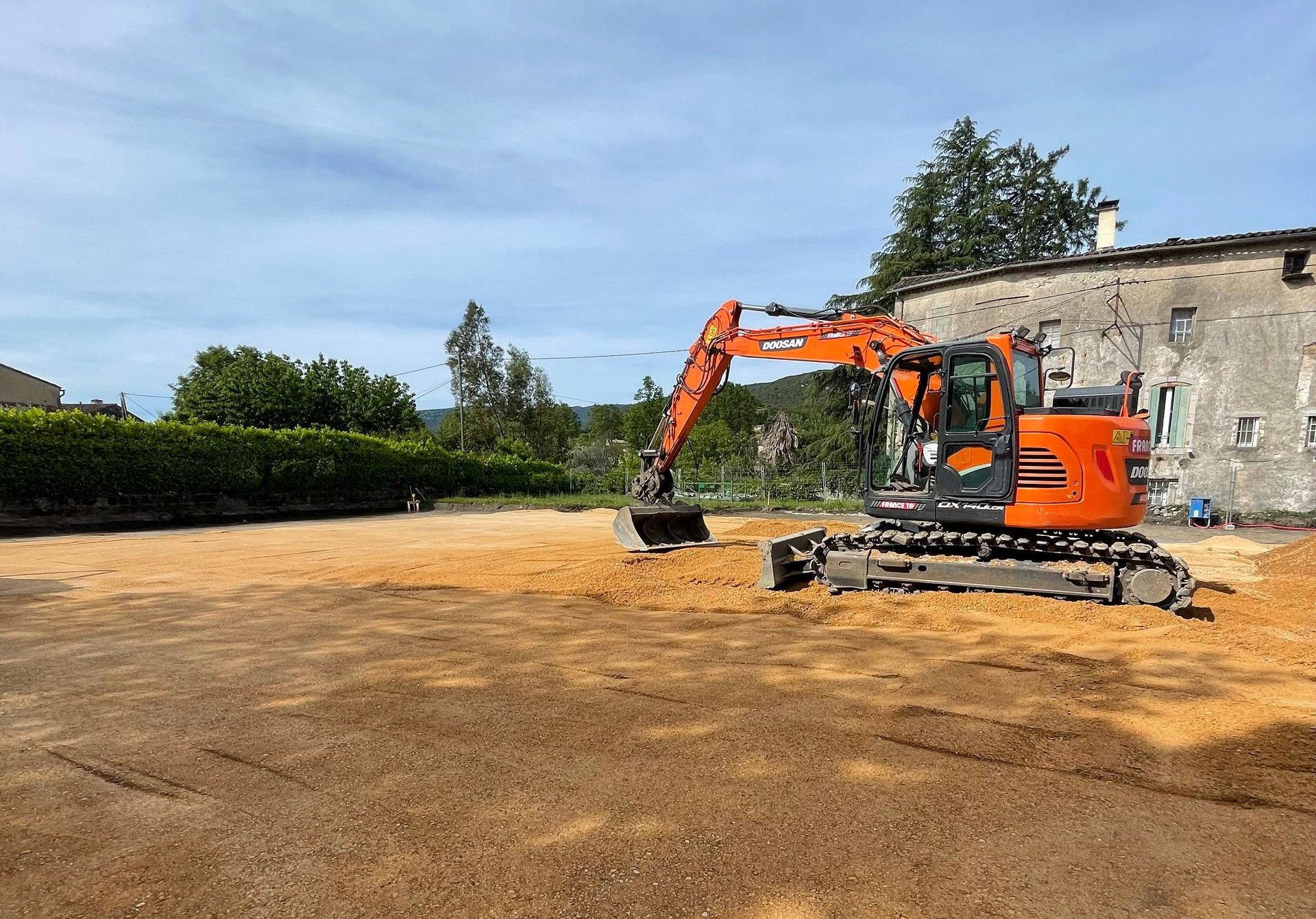 Une pelleteuse orange prépare un terrain pour des travaux de construction.