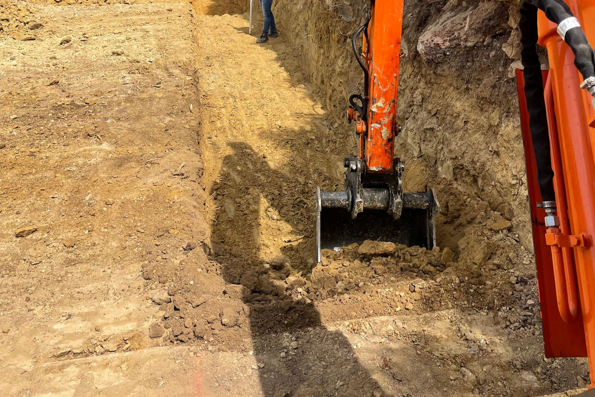 Une pelleteuse orange creuse une tranchée sur un chantier de construction en terre.