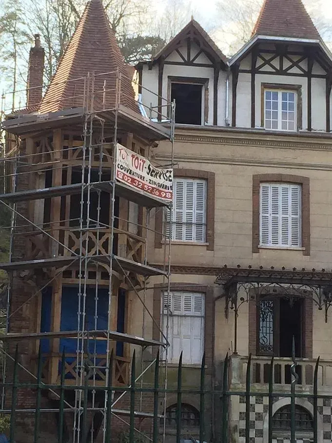 Le haut d'une maison avec une fenêtre ouverte et un échafaudage de l'entreprise Toit Service