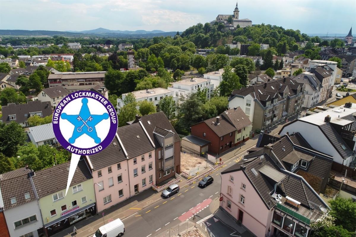 Stadtansicht mit einem Gebäude mit einem blauen Logo und einem Stern; im Hintergrund Gebäude und eine Burg auf einem Hügel.