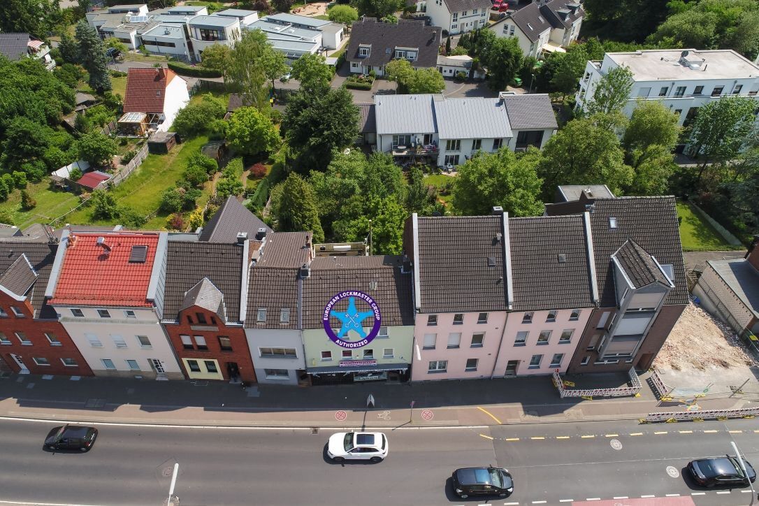 Reihe bunter Gebäude mit geparkten Autos auf einer Straße darunter. Grüne Bäume und Häuser im Hintergrund.