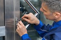 Mann in blauer Uniform knackt mit kleinen Werkzeugen ein Türschloss.