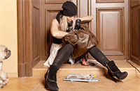 Frau mit schwarzer Mütze und Stiefeln sucht in einer braunen Tasche vor der Tür.