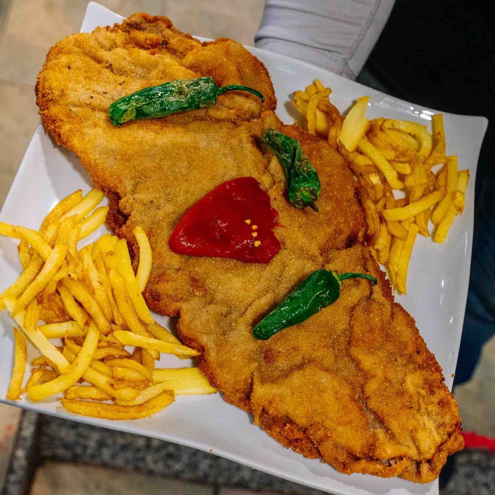 Chuleta empanizada frita con papas fritas y salsa roja en un plato blanco.