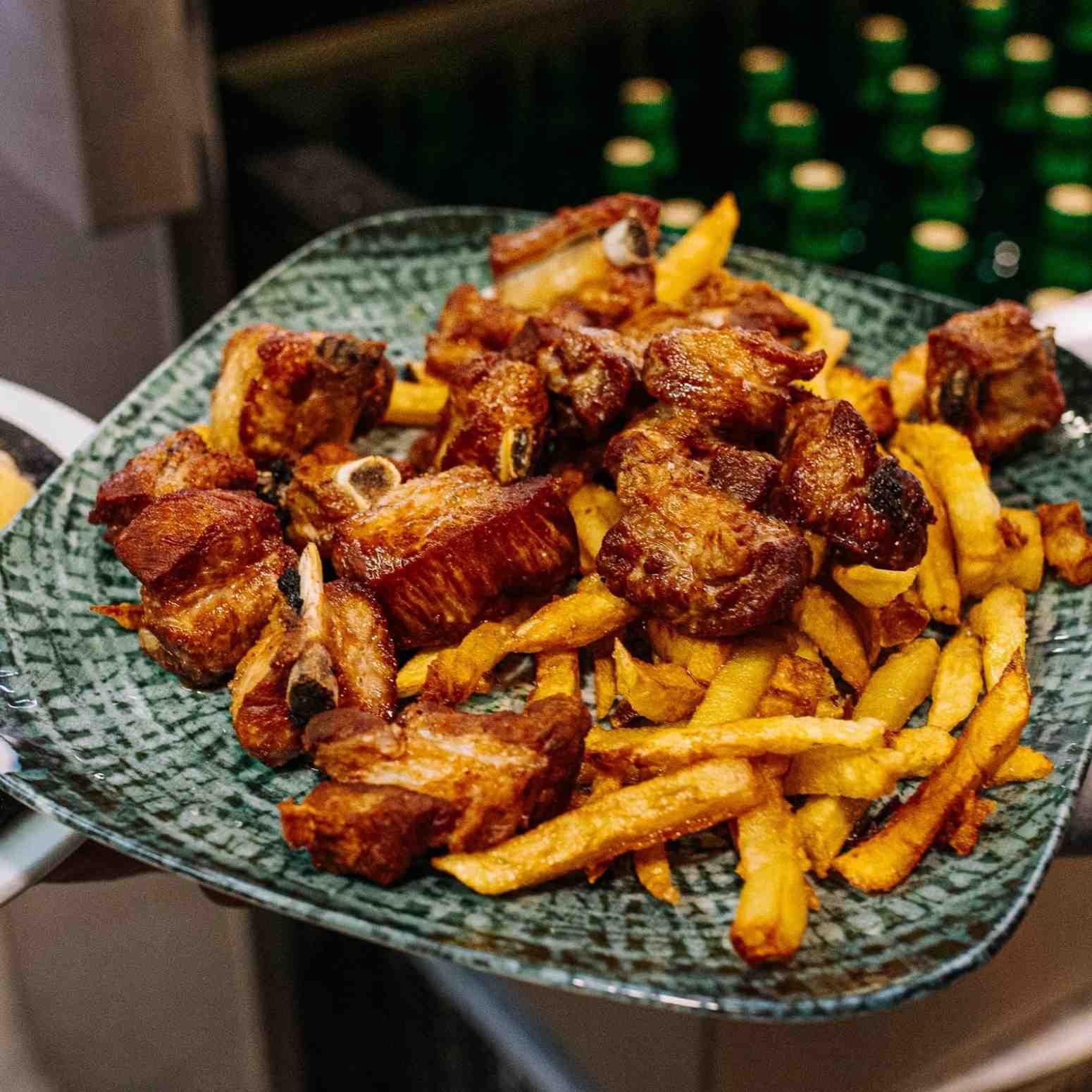 Plato de alitas de pollo fritas y patatas fritas en una bandeja tejida verde.