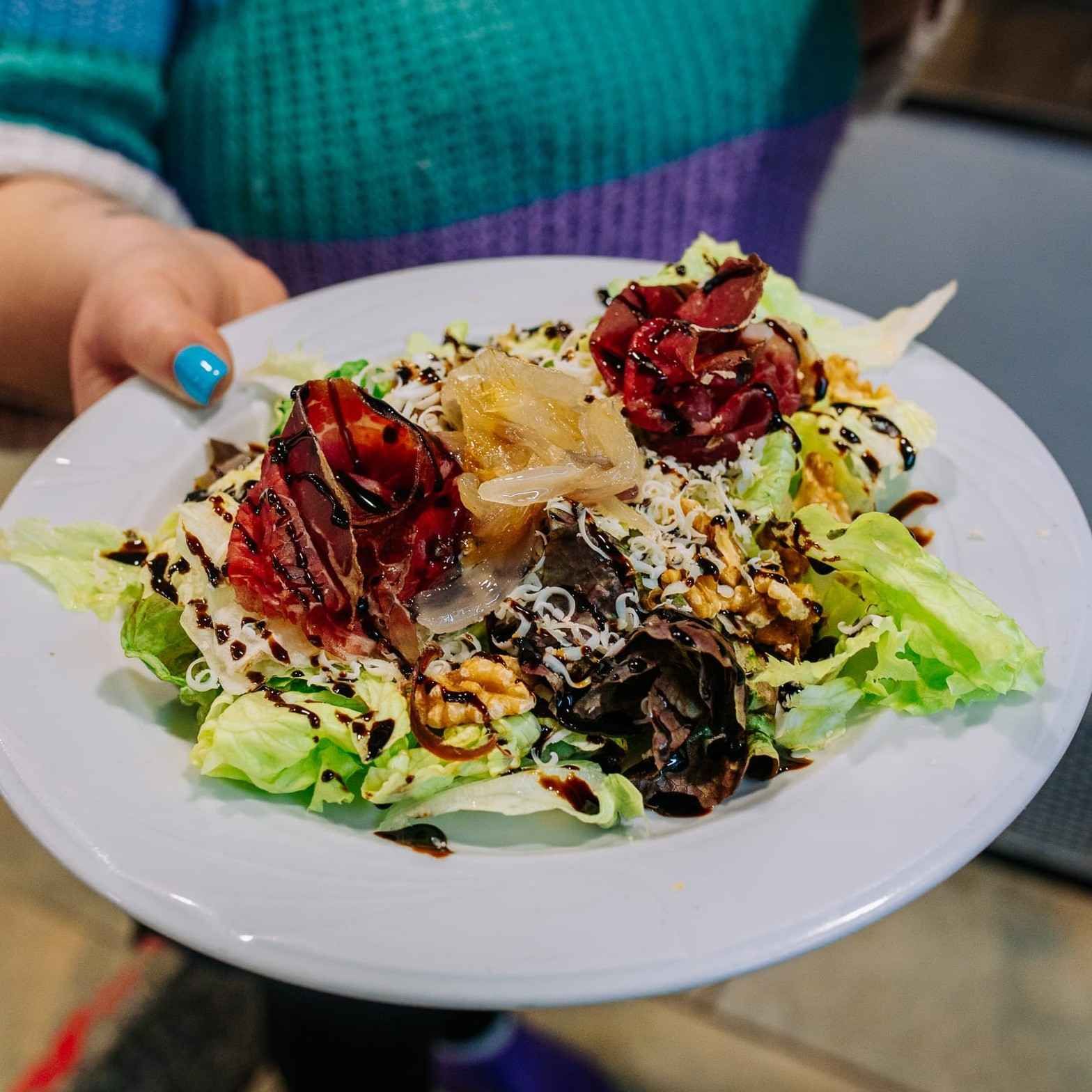 Una mano sostiene un plato de ensalada con remolacha roja, queso, nueces y aderezo balsámico.