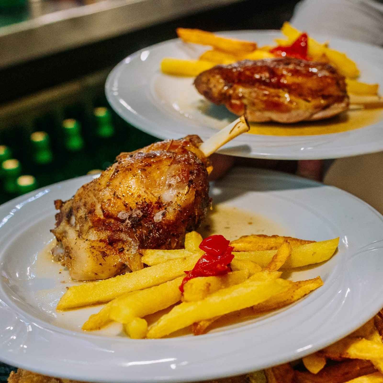 Muslos de pollo a la parrilla emplatados con papas fritas y guarnición roja en un ambiente de cocina.