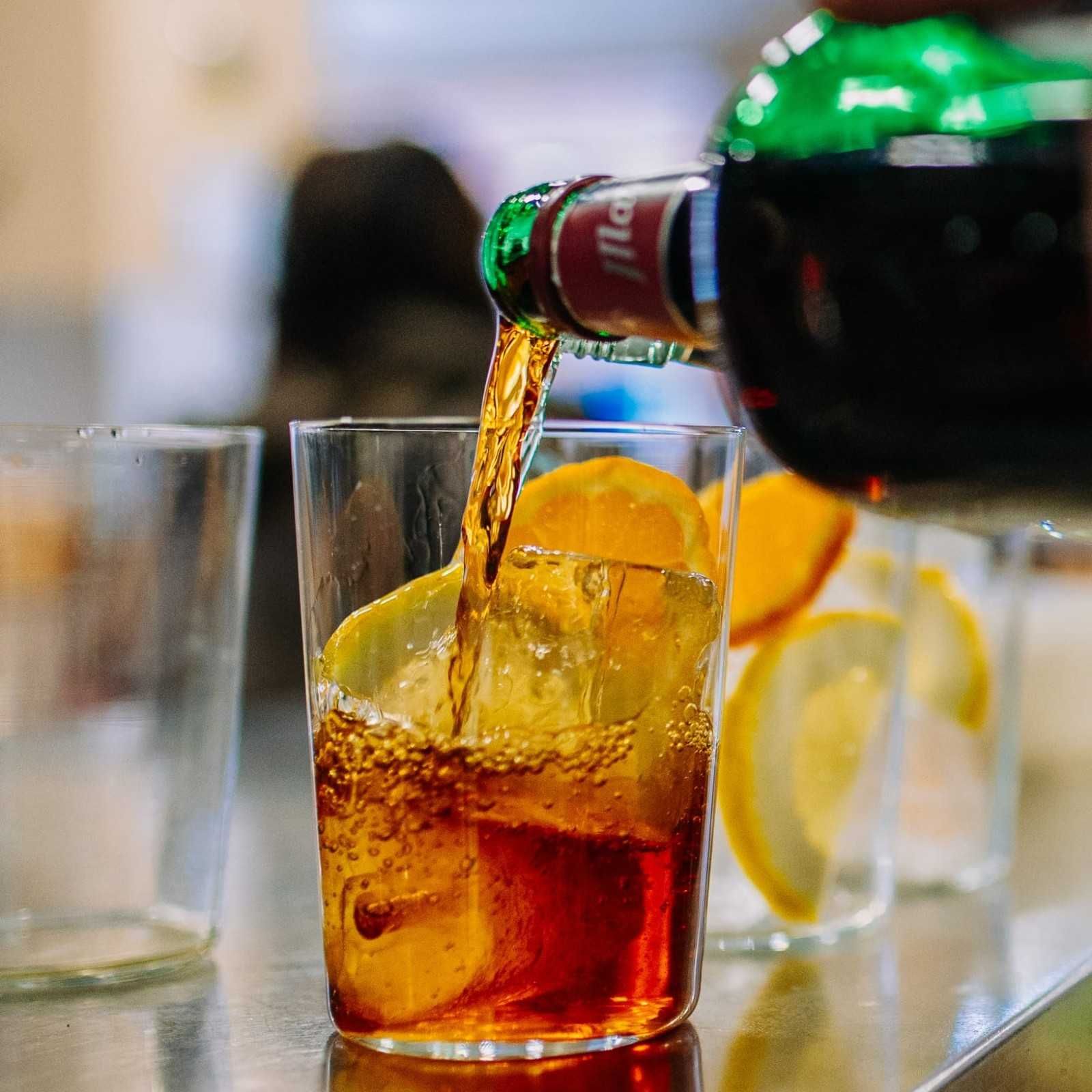 Se sirve cola en un vaso con hielo y rodajas de limón sobre una mesa.