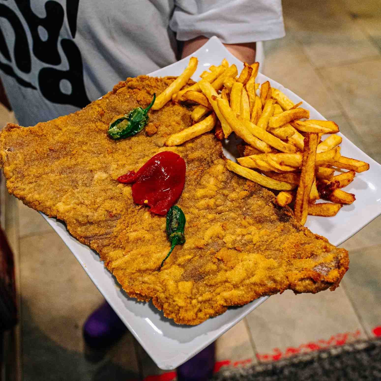 Escalope grande empanizado en una bandeja con papas fritas y kétchup, servido en un restaurante informal.