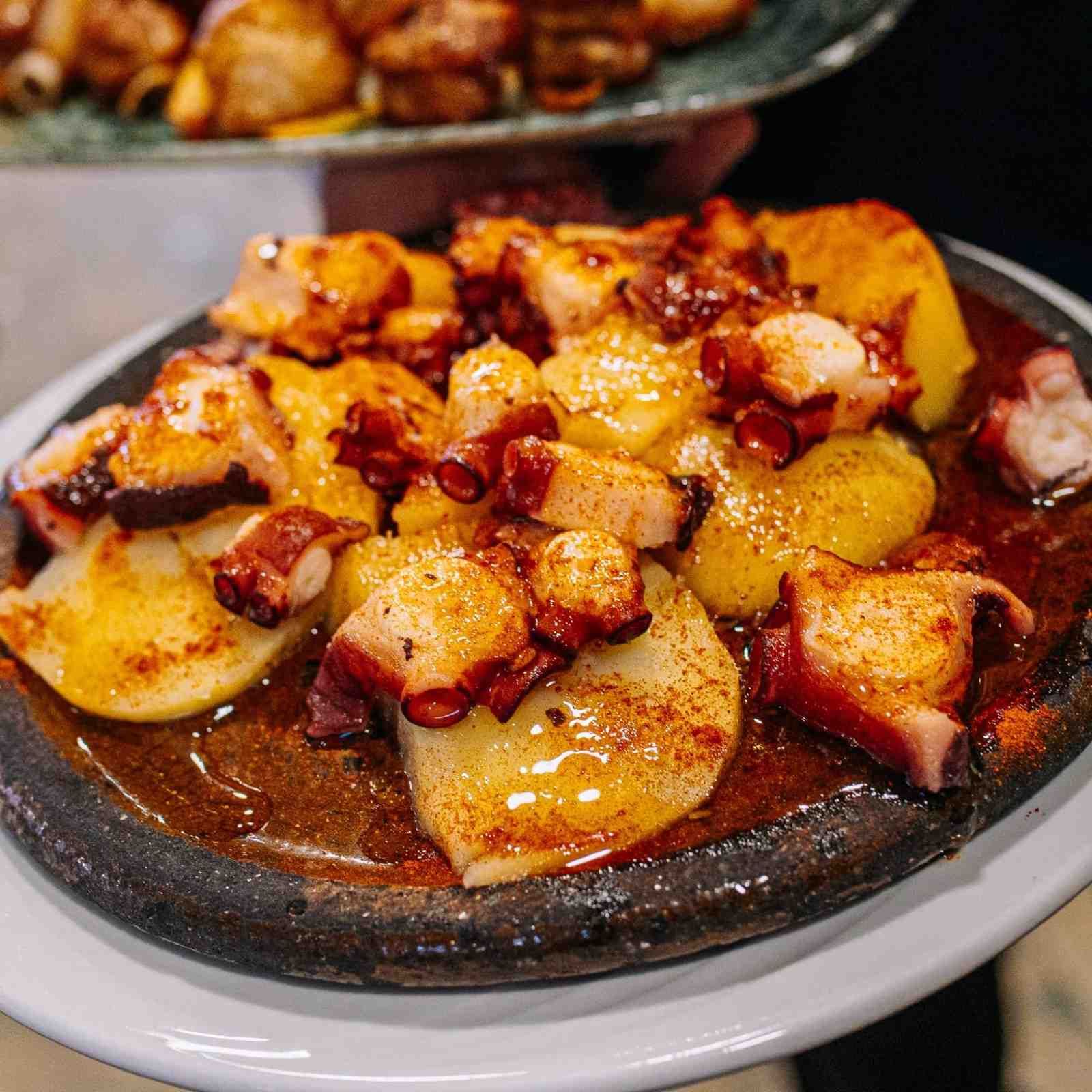 Patatas asadas emplatadas con trocitos de beicon crujiente y salsa en un plato oscuro.