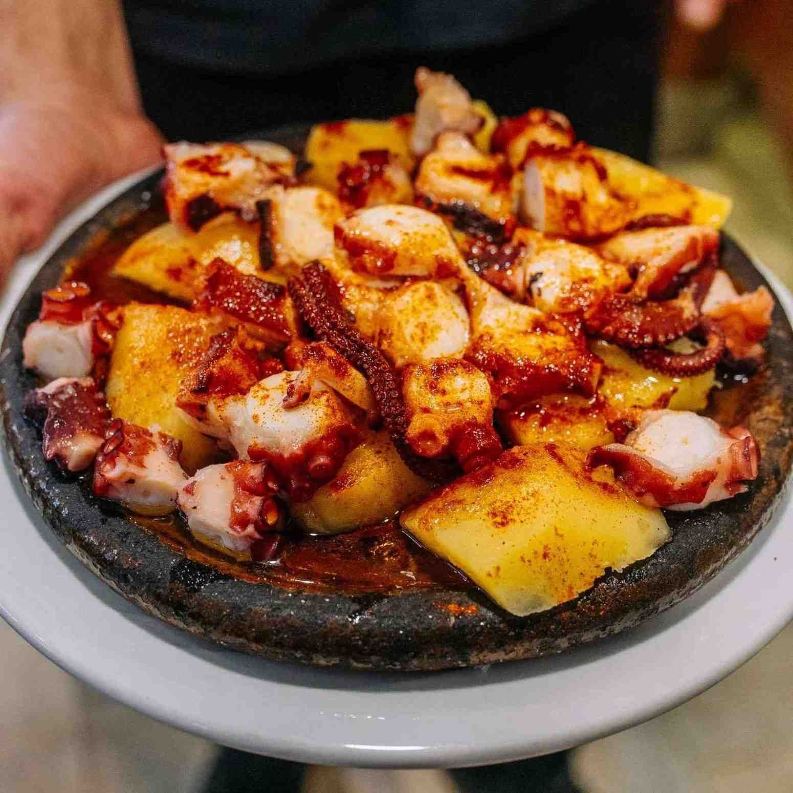 Plato de pulpo a la parrilla y patatas con salsa roja sobre un plato blanco.