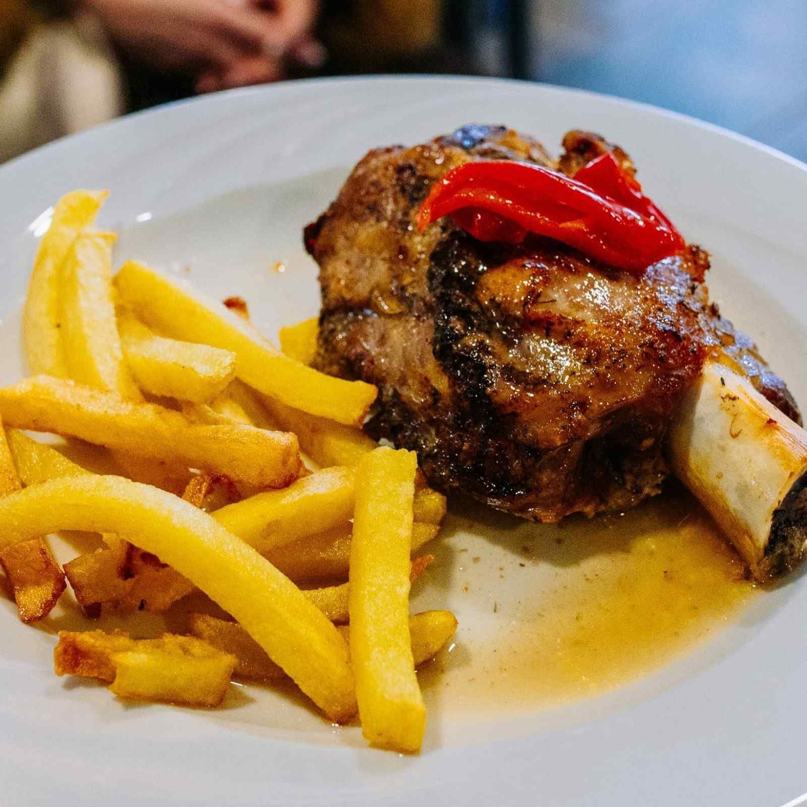 Plato con papas fritas y un plato de carne a la parrilla cubierto con pimientos rojos.