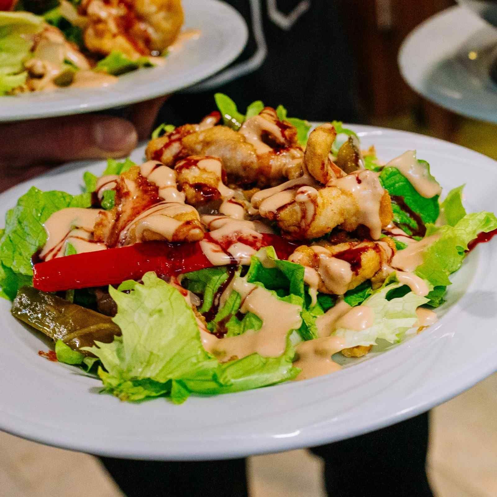 Ensalada con pollo a la parrilla, lechuga y pimiento rojo en un plato blanco en la mesa de un restaurante.