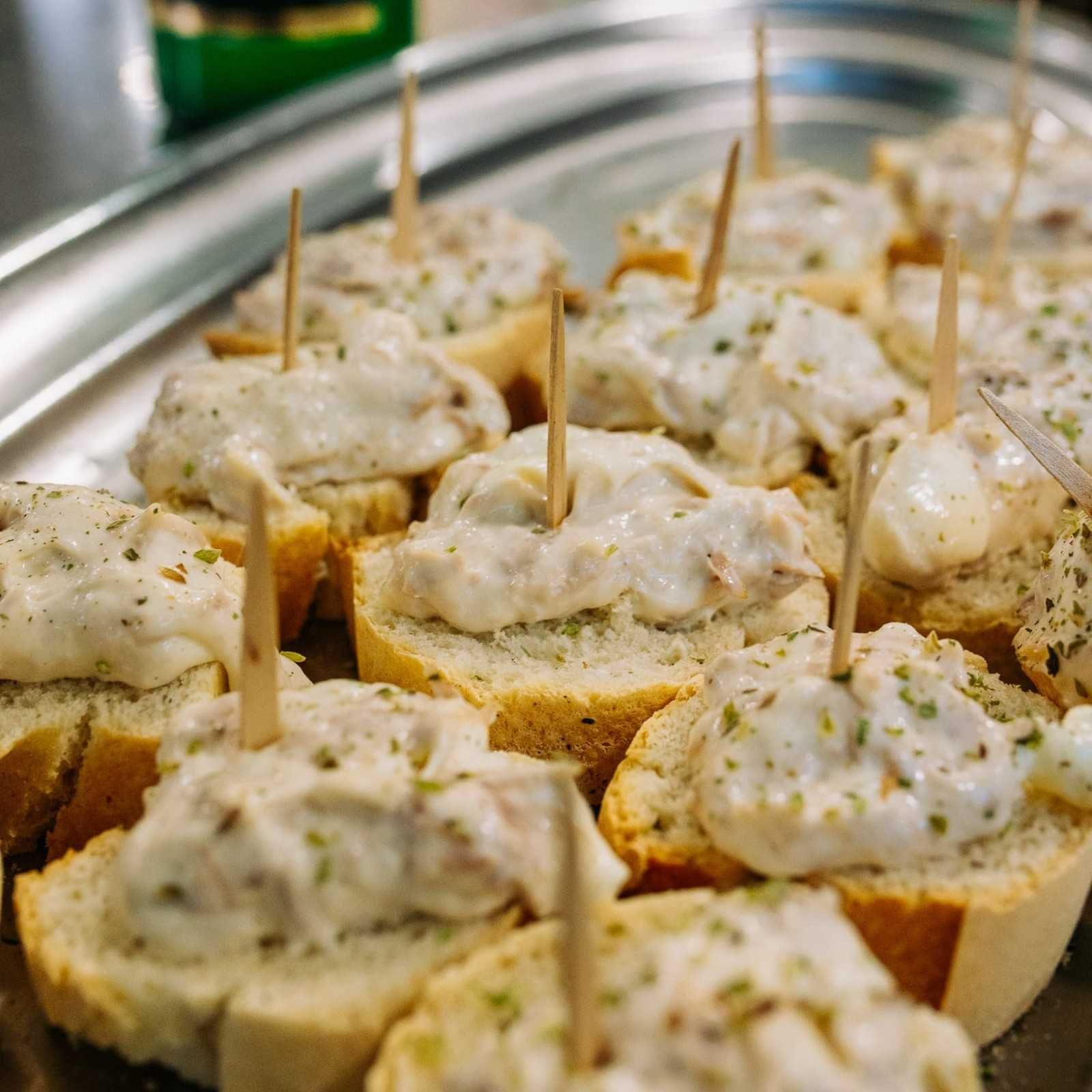 Bocaditos de pan ensartados en palillos y cubiertos con una crema para untar, presentados en una bandeja.
