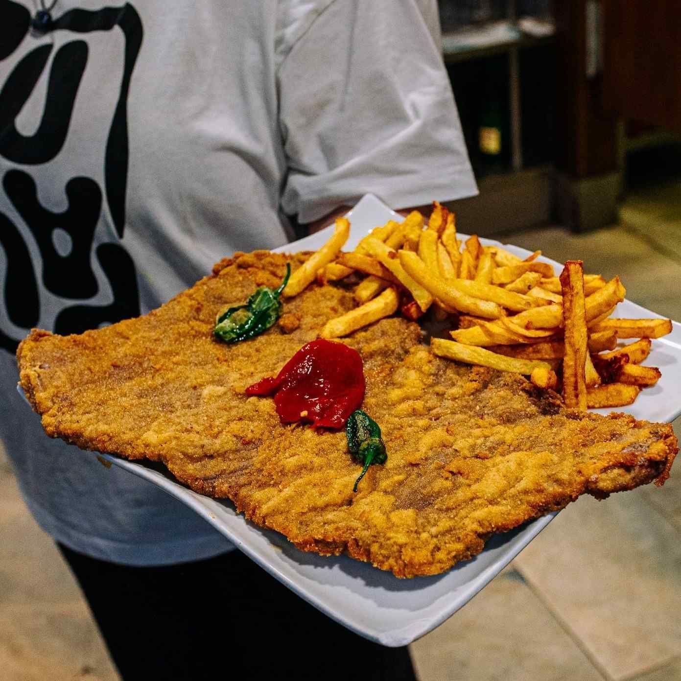 Bandeja con una chuleta grande empanizada y frita, papas fritas y ketchup sobre el regazo de una persona.