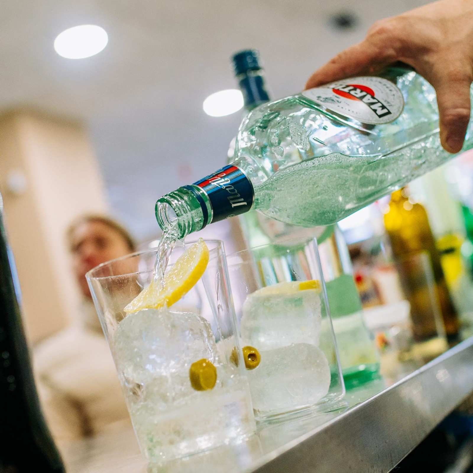Un camarero sirve licor transparente en copas de cóctel adornadas con lima en un bar.