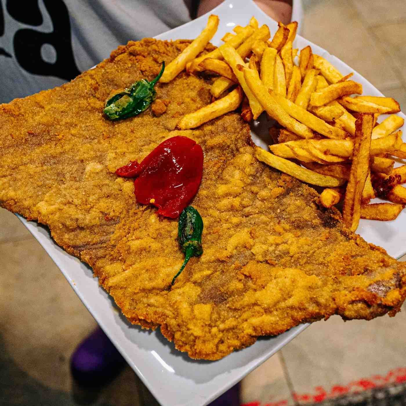 Escalope empanizado frito con papas fritas y pimientos rojos y verdes en un plato blanco.