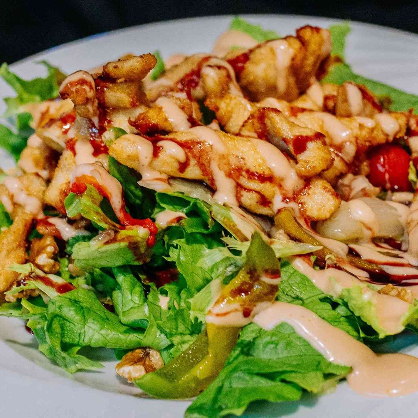 Ensalada fresca con tiras de pollo a la parrilla, rociada con aderezo cremoso en un plato blanco.