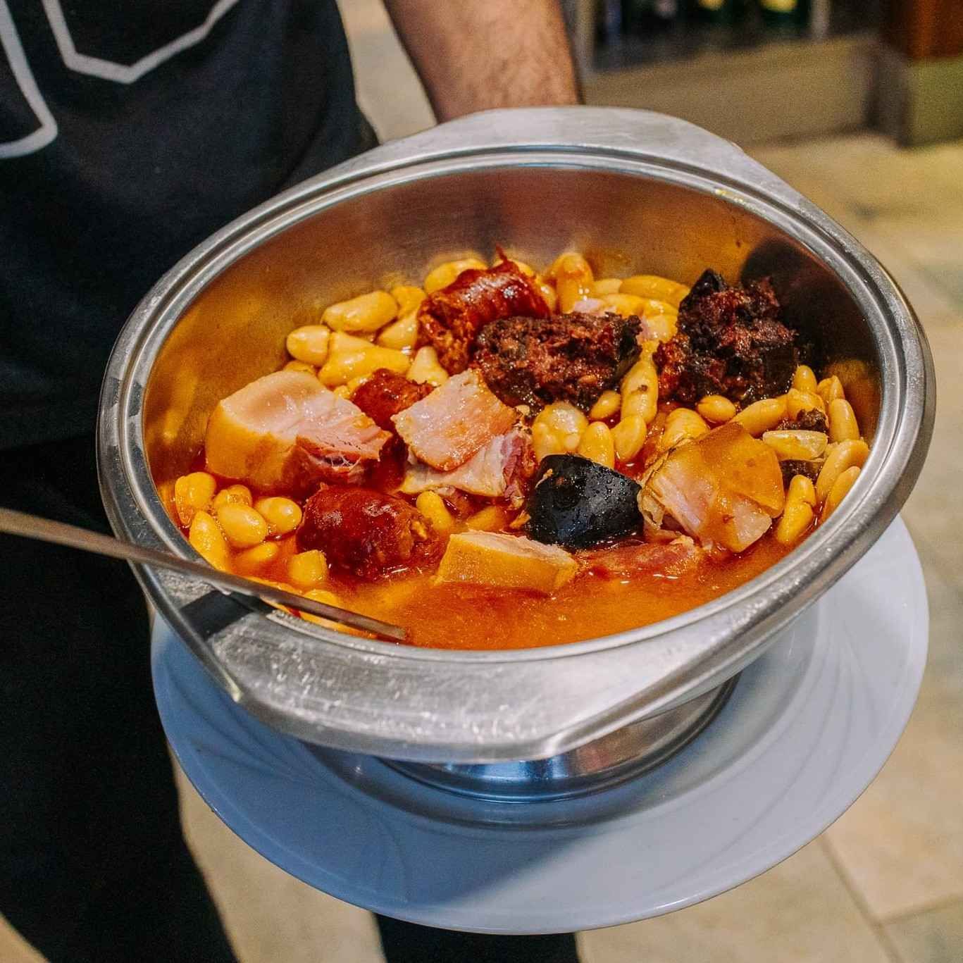 Bol de metal con estofado de garbanzos, trozos de carne y salsa en un plato.