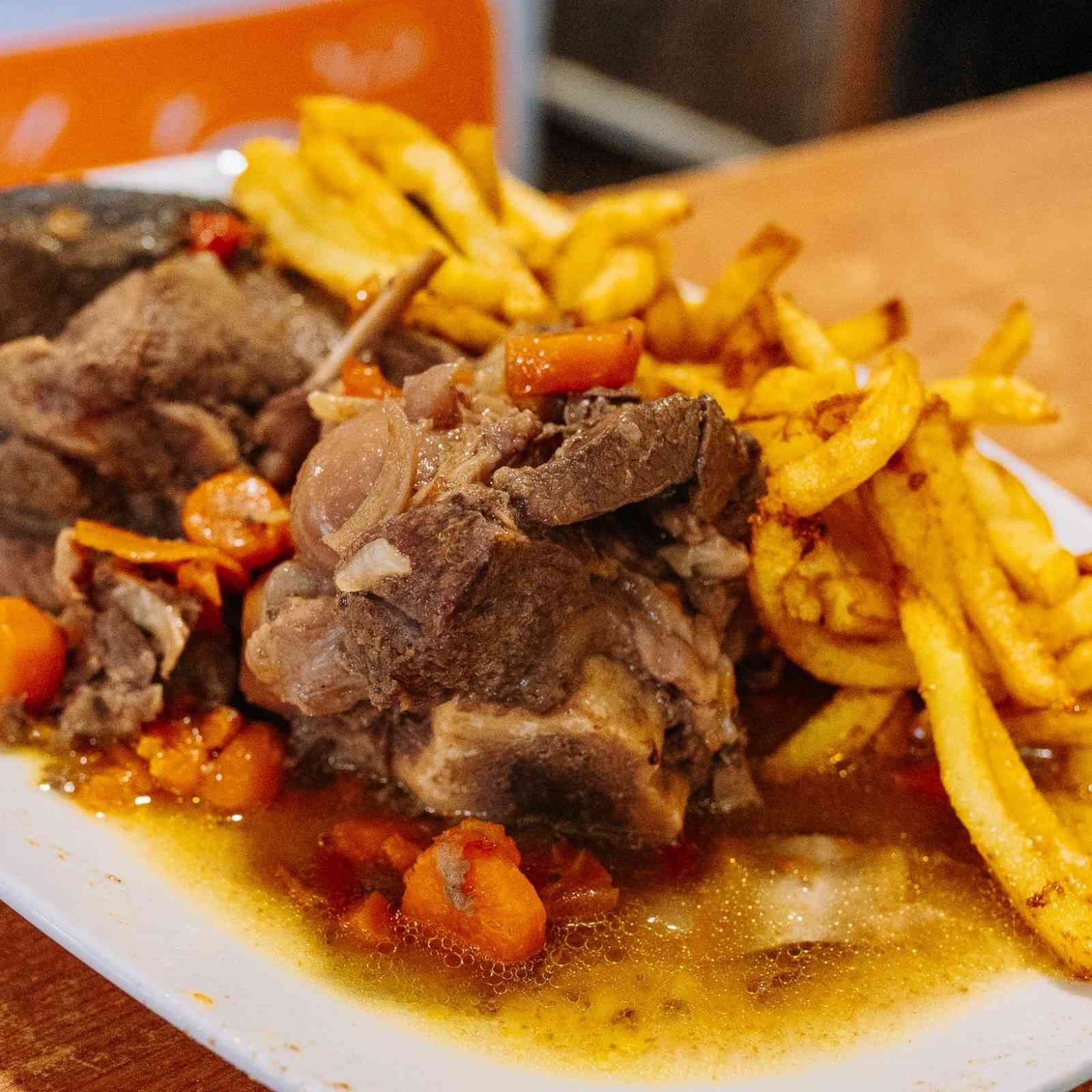 Plato de carne con patatas fritas y salsa en un plato blanco.