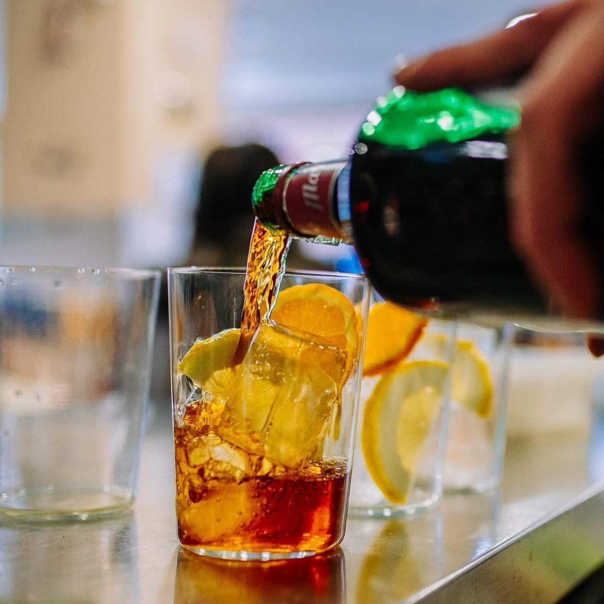 En la barra de un bar, se vierte refresco en un vaso con hielo y rodajas de limón.