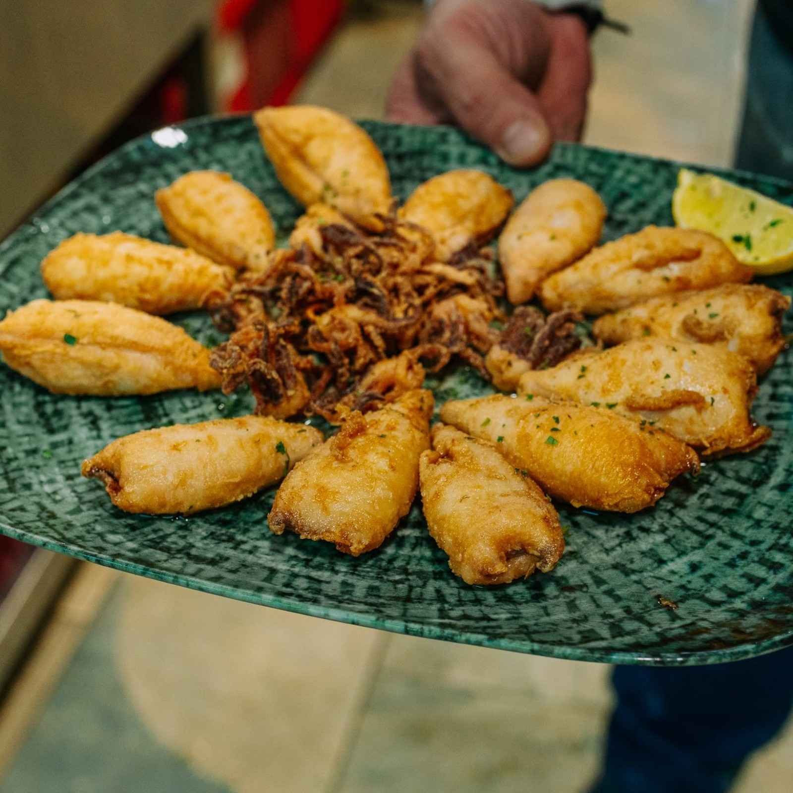 Plato de empanadillas fritas dispuestas alrededor de cebollas crujientes en una fuente con estampado verde.
