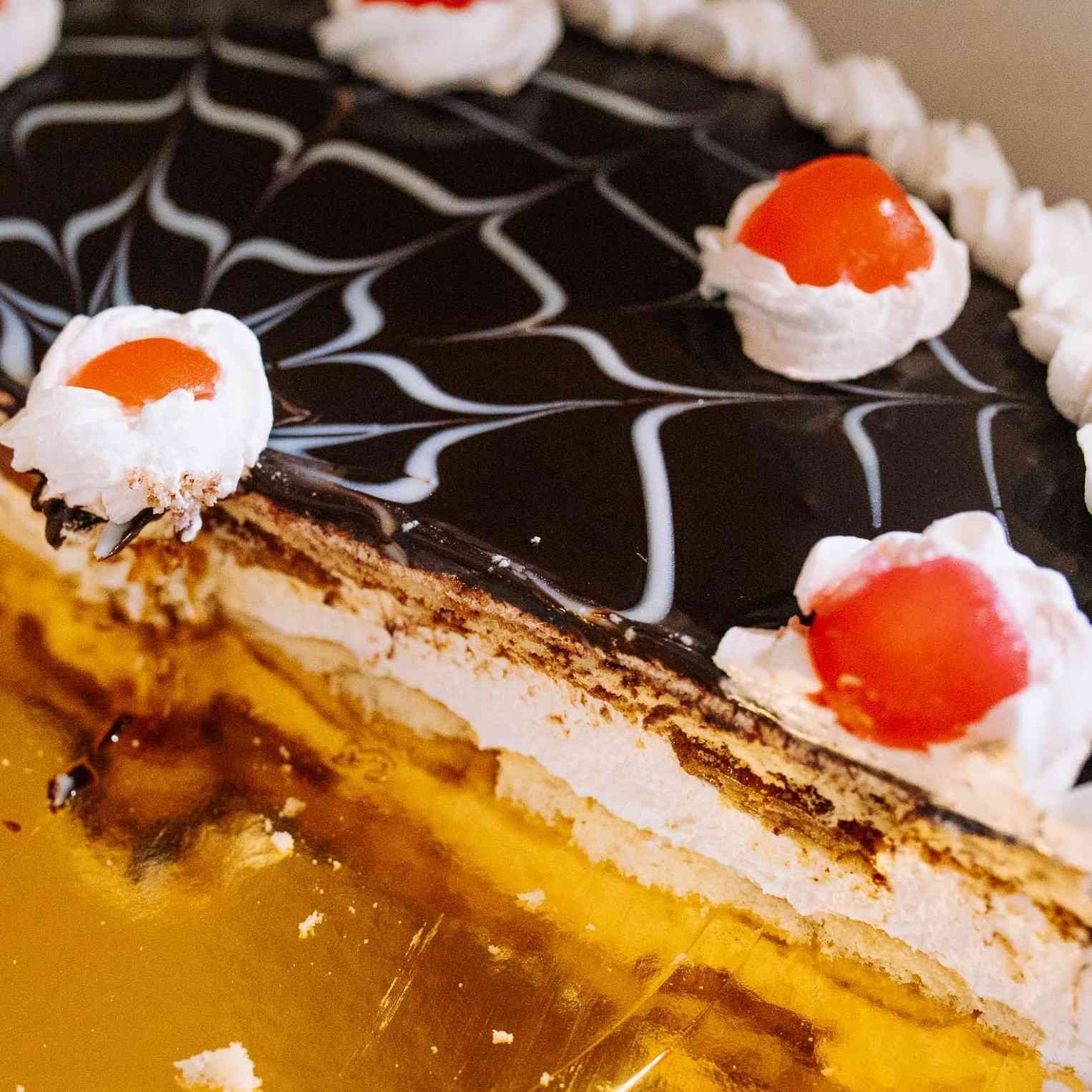 Rebanada de pastel de chocolate y crema en capas con sirope de chocolate blanco y cobertura de cerezas rojas.