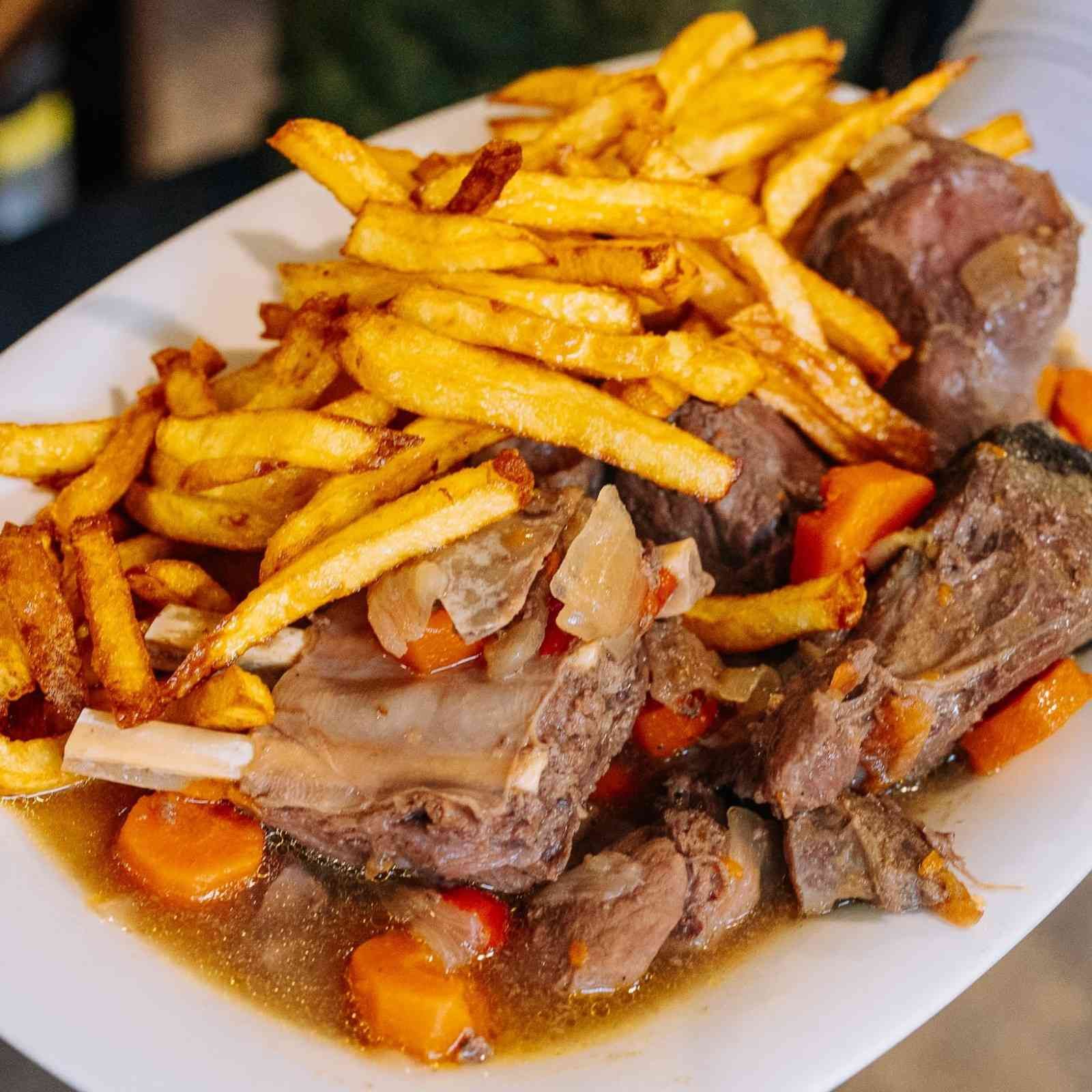 Plato de estofado con carne y verduras, coronado con patatas fritas crujientes.