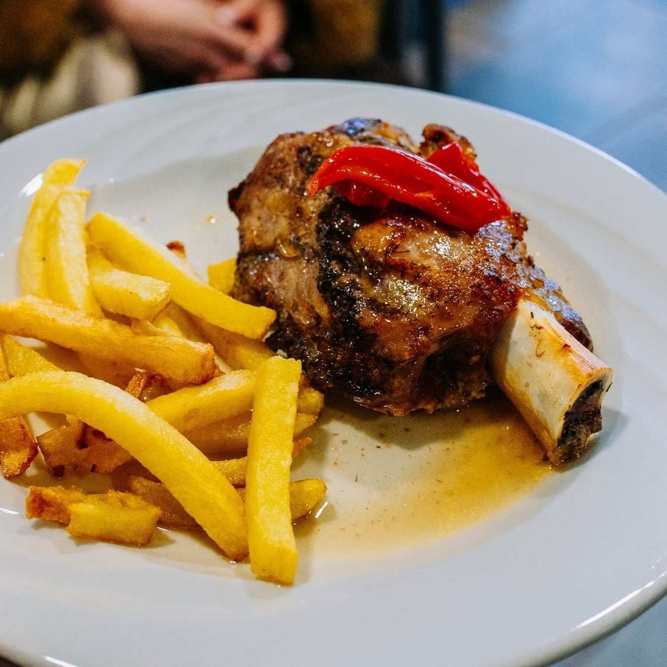 Plato de patatas fritas con carne a la parrilla, pimientos rojos y un hueso sobre un plato blanco.
