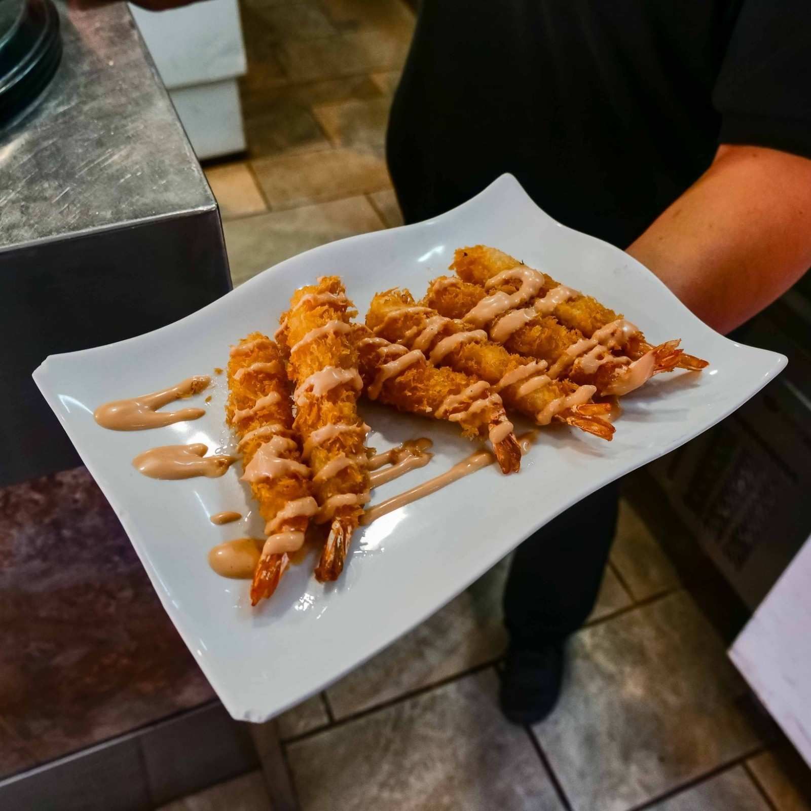 Plato de tiras de postre fritas rociadas con salsa de caramelo, sostenido por un camarero en un restaurante.