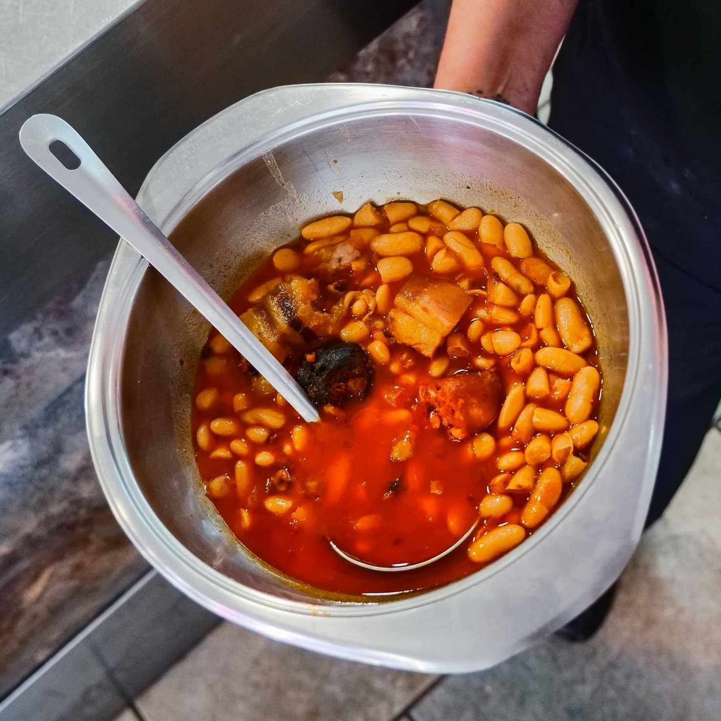 Una olla metálica con sopa de frijoles de caldo rojo y una cuchara dentro.