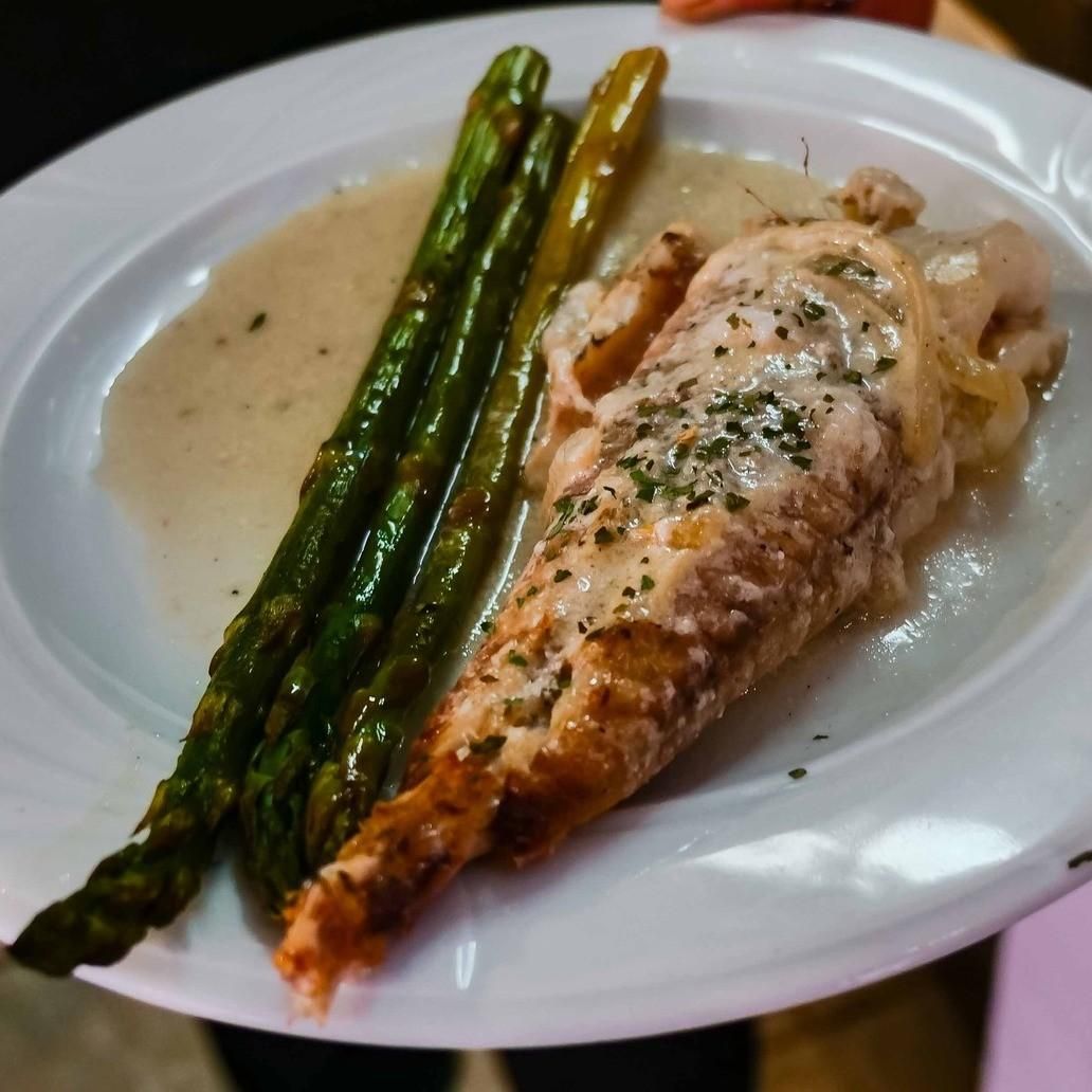 Salmón a la parrilla con espárragos en un plato blanco, cubierto con hierbas y salsa ligera.