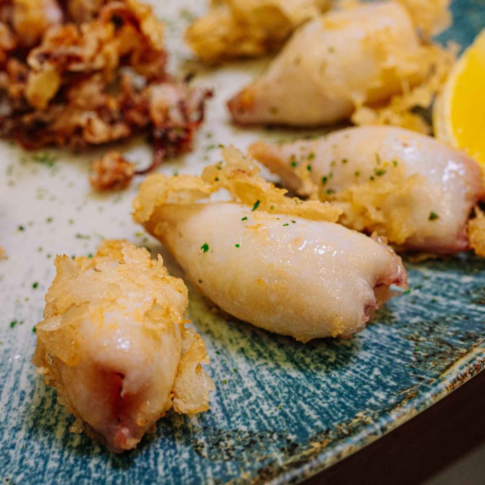 Trozos de calamar a la parrilla presentados en un plato de cerámica azul, adornados con hierbas y servidos con rodajas de limón.