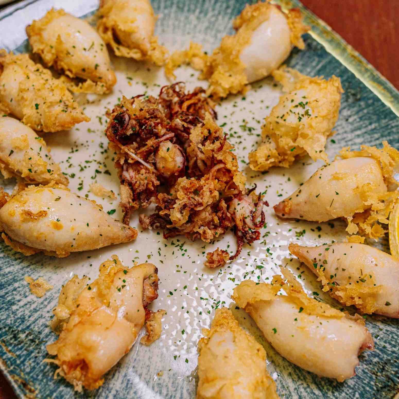 Plato de empanadillas doradas fritas dispuestas alrededor de una salsa picante para mojar en el centro, espolvoreadas con hierbas.