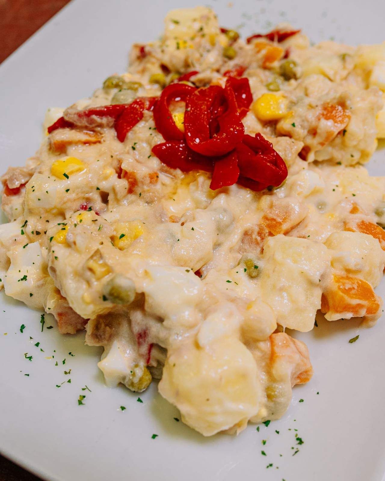 Ensalada cremosa de patatas con rodajas de pimiento rojo sobre un plato blanco.