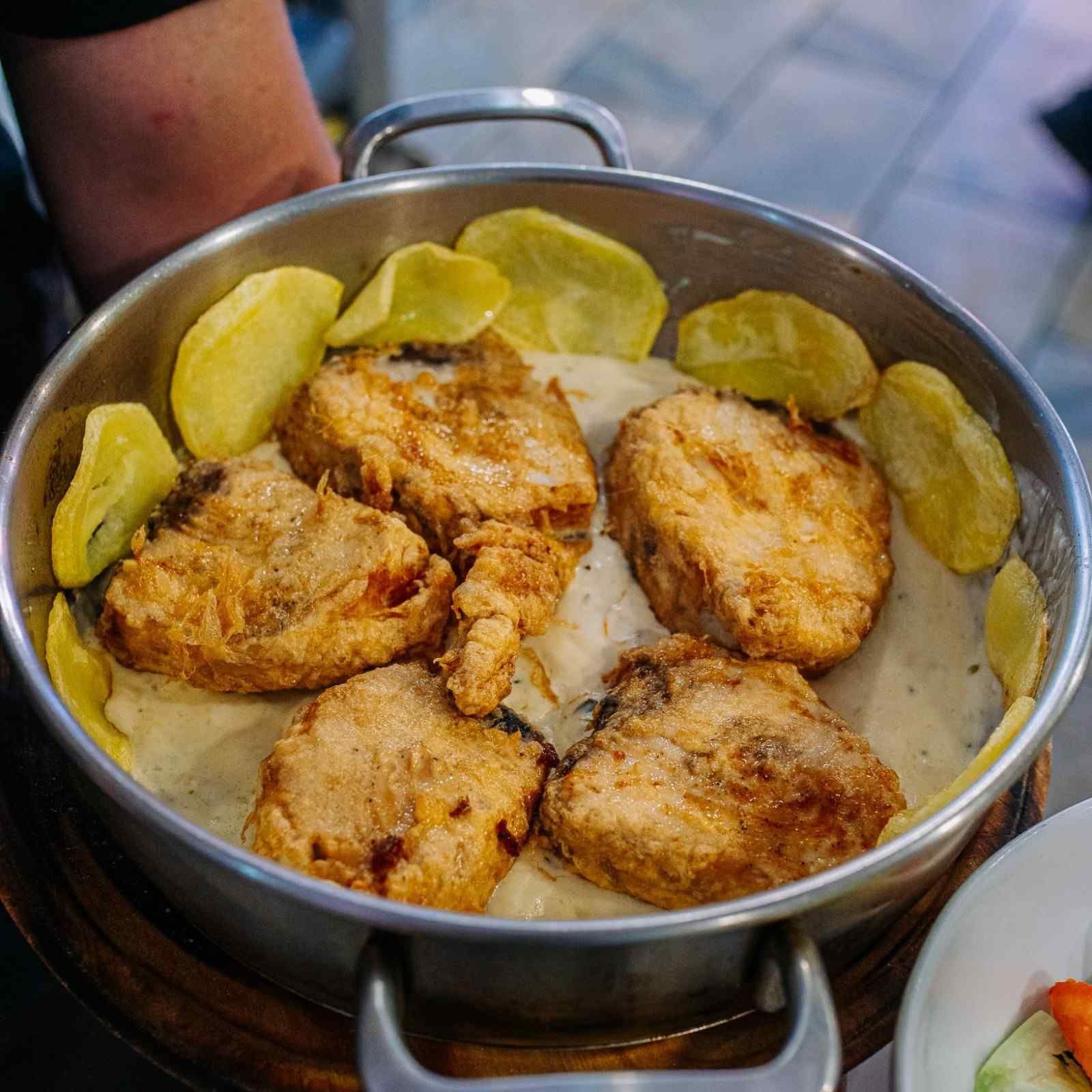 Olla con trozos de pollo asado y rodajas de patata dispuestas alrededor.
