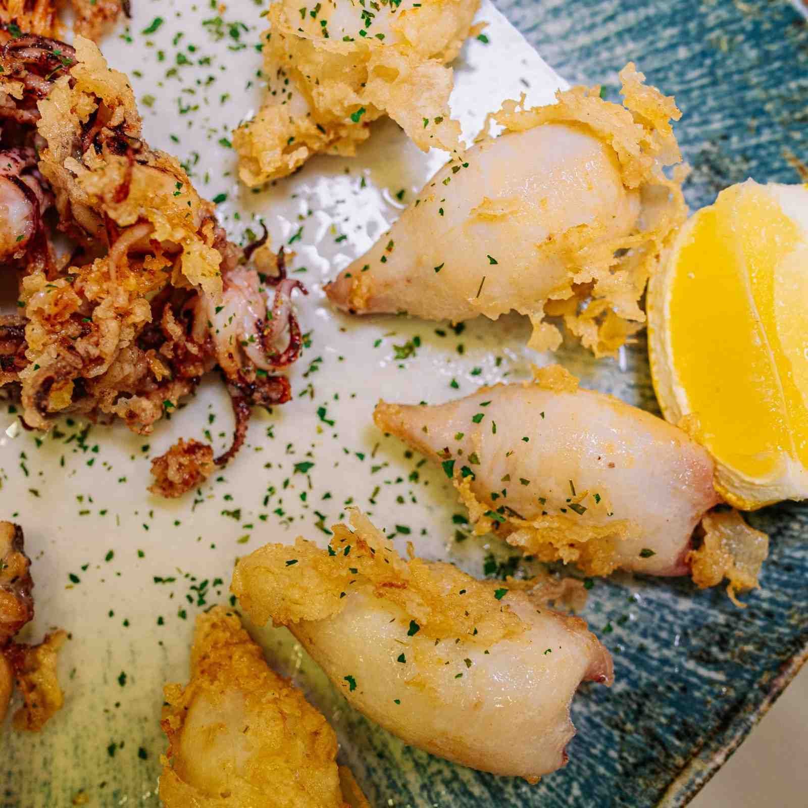 Mariscos emplatados con rodajas de limón y guarnición de hierbas en un plato azul.