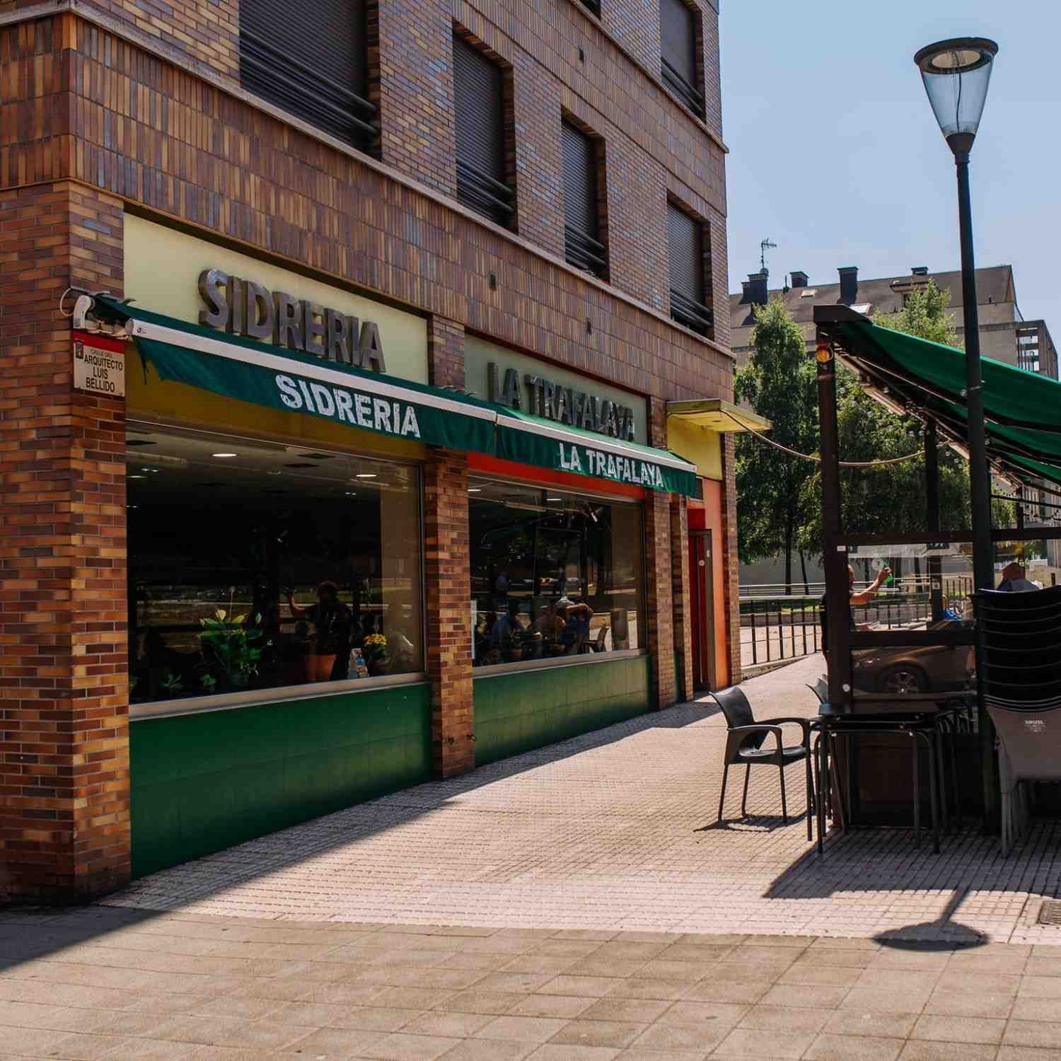 Local comercial en esquina con toldo verde y fachada de ladrillo en una soleada calle peatonal.