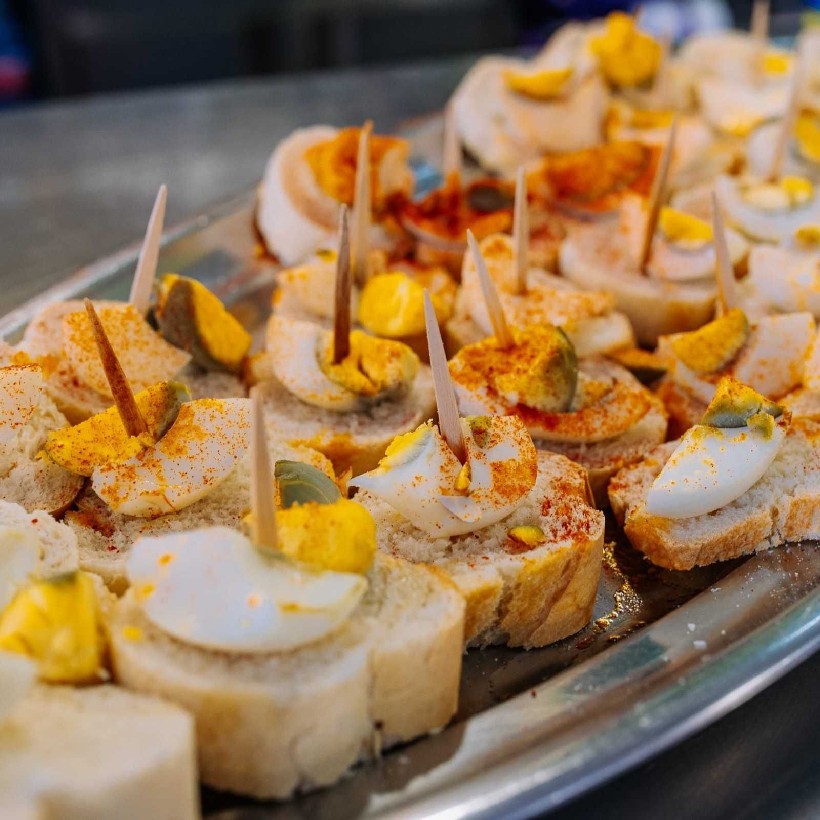 Canapés de ensalada de huevo sobre rebanadas de pan, espolvoreados con pimentón y palillos de dientes en una bandeja de servir.