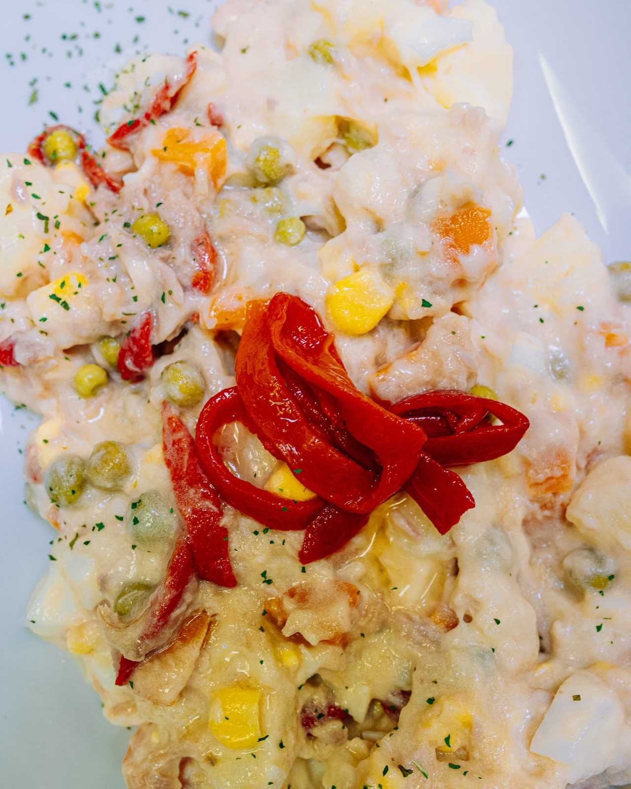 Arroz cremoso cubierto con tiras de pimiento rojo y verduras mixtas.