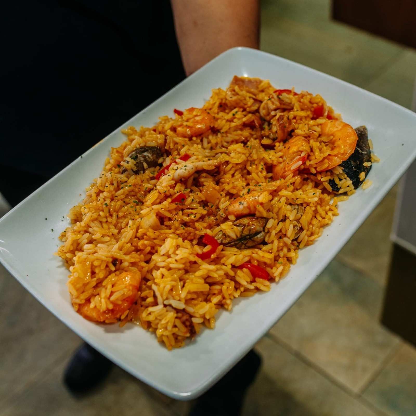 Plato de arroz naranja con camarones y salsa en un plato rectangular blanco.