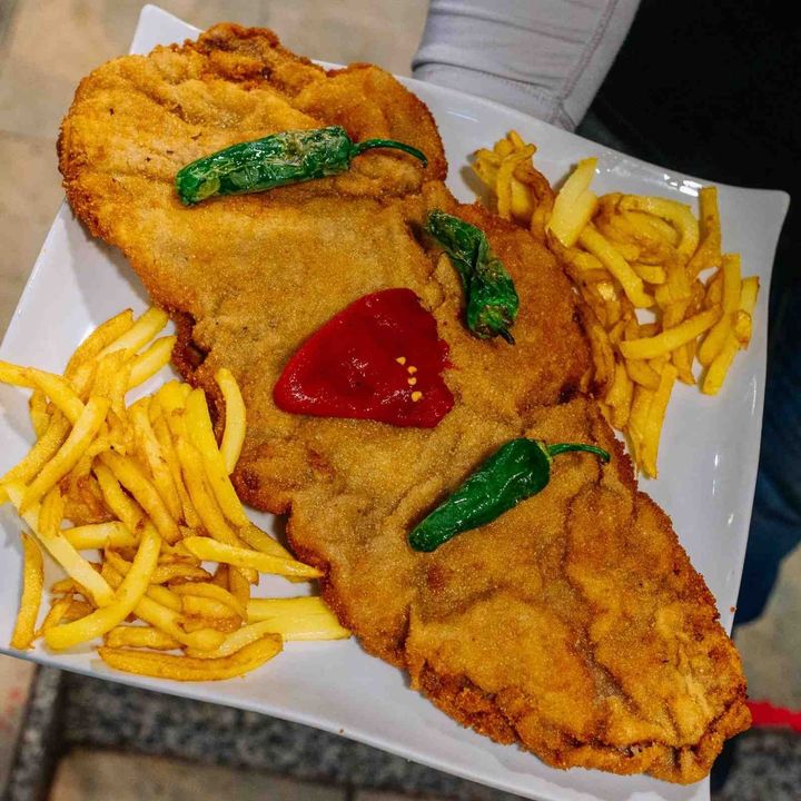 Escalope empanado con patatas fritas y kétchup, cubierto con pimientos verdes en un plato.
