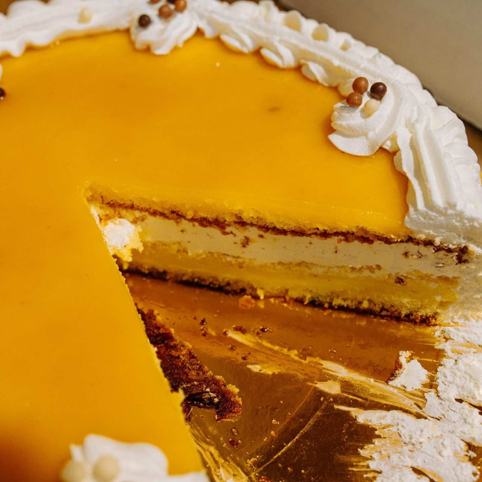 Rebanada de pastel glaseado amarillo con crema batida blanca en un plato.