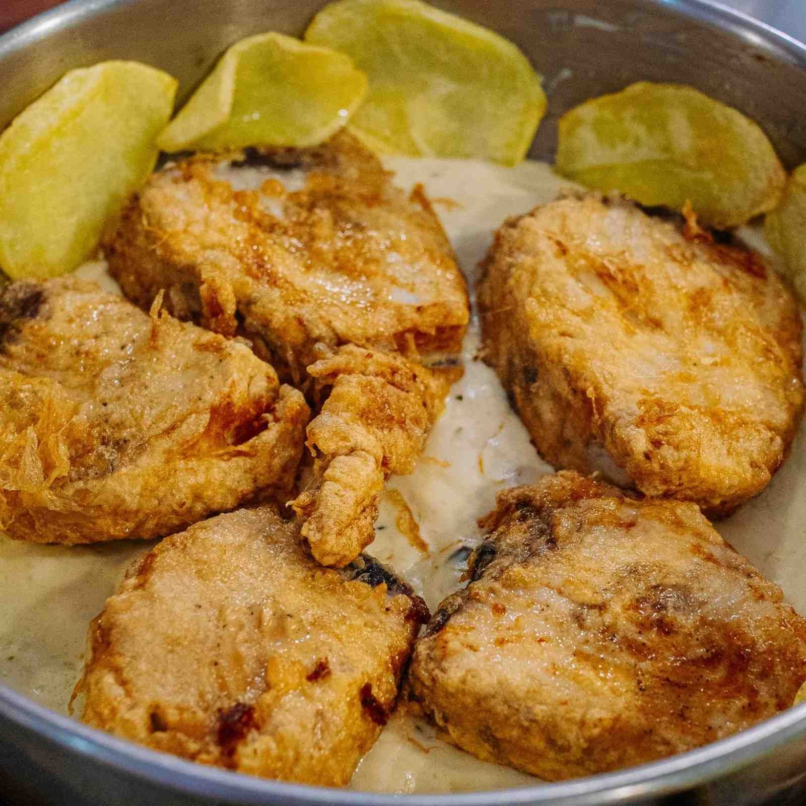 Filetes de pescado fritos en una sartén con rodajas de lima dispuestas alrededor.